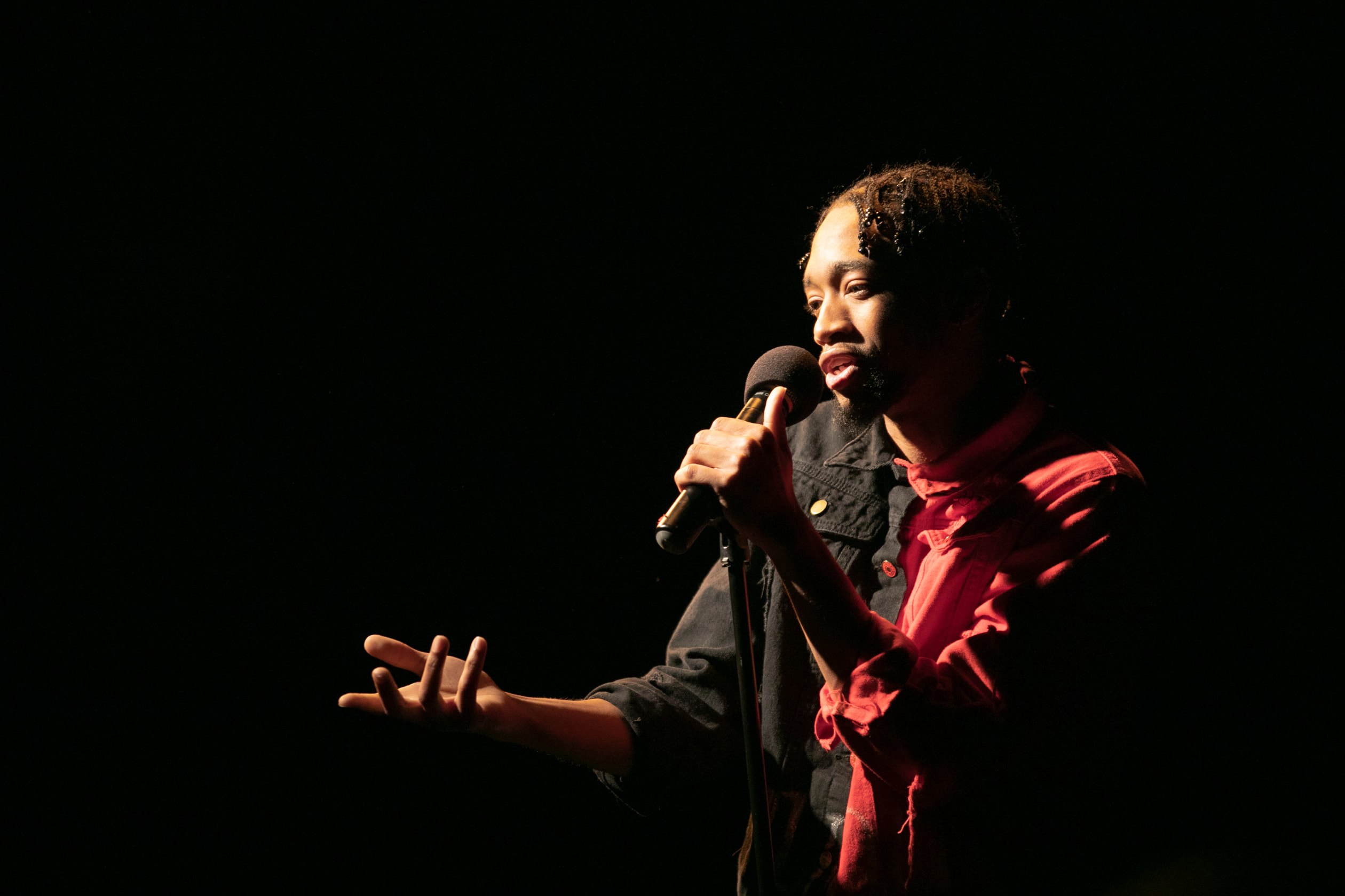 A singer gestures with one arm forward and the other holding the stand of a microphone