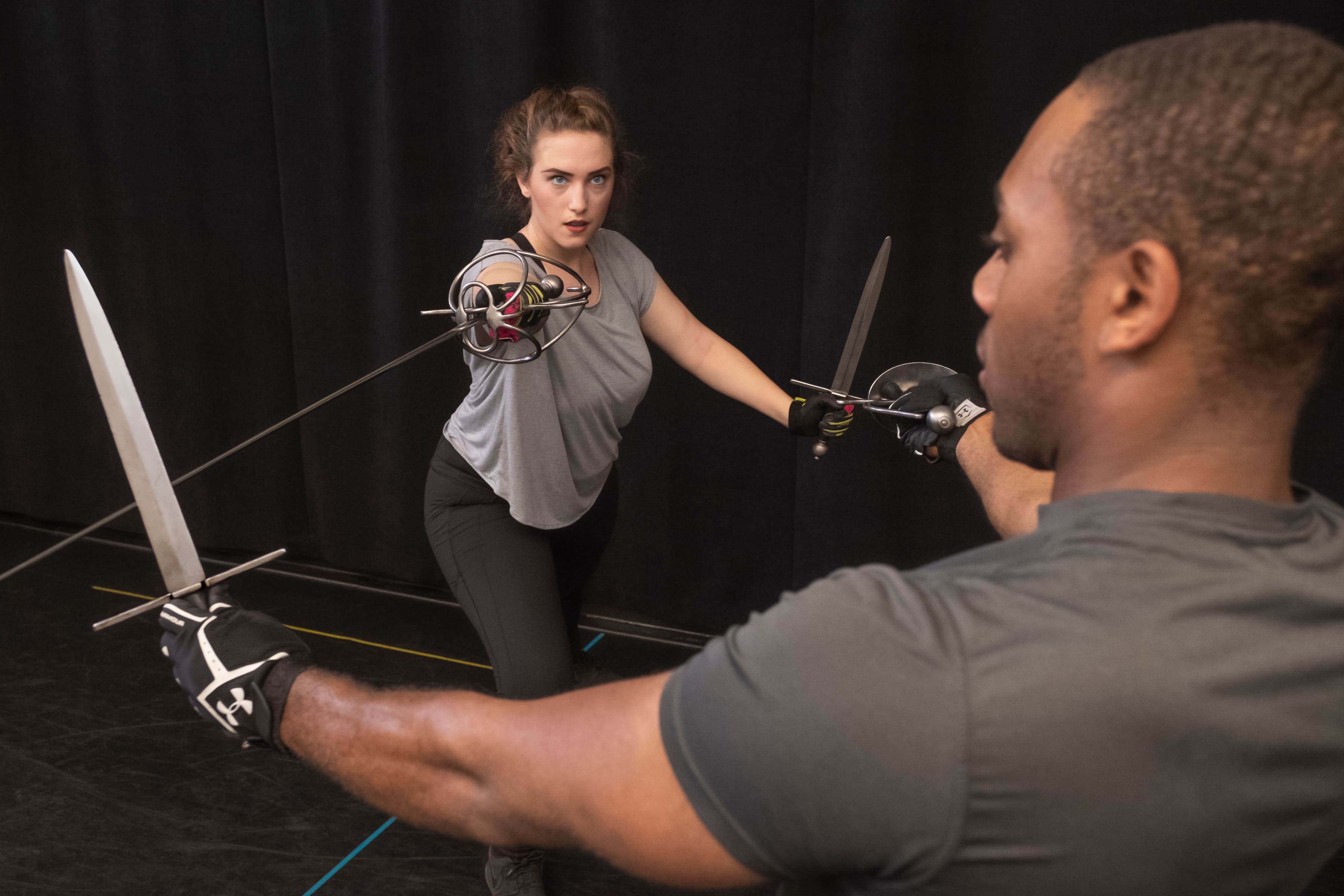 Two rehearsing performers train in stage combat with rapiers and parrying swords