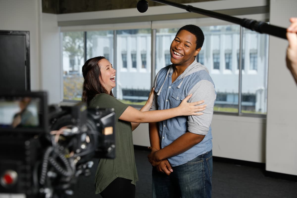 Two actors share a laugh in front of the camera