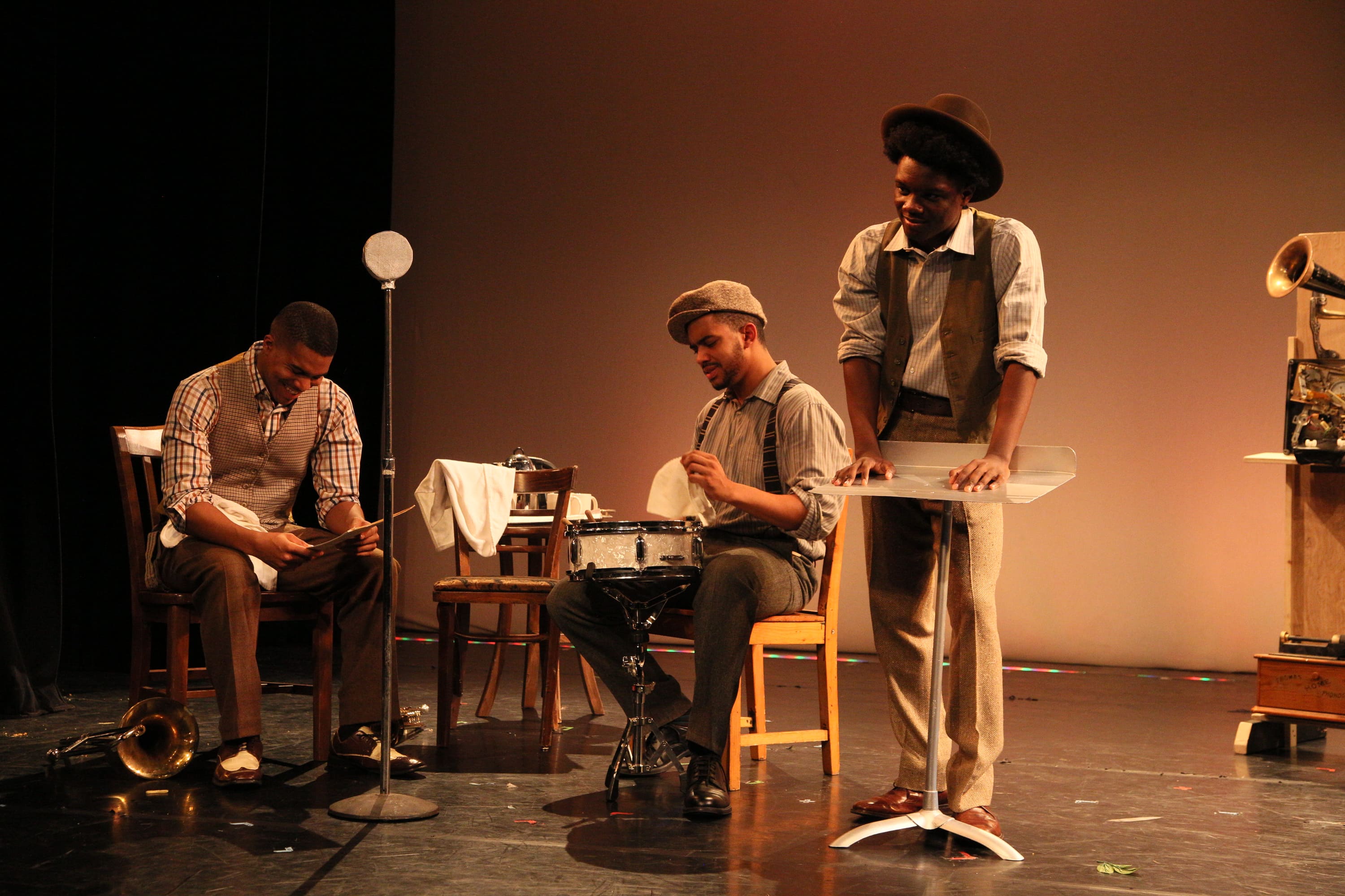 Three band members on stage with various instruments appear to be taking a break from rehersal