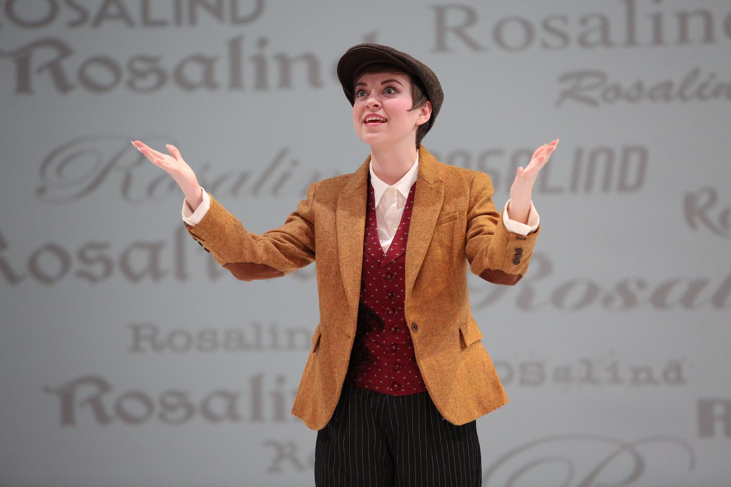 actor with pageboy hat raises arms