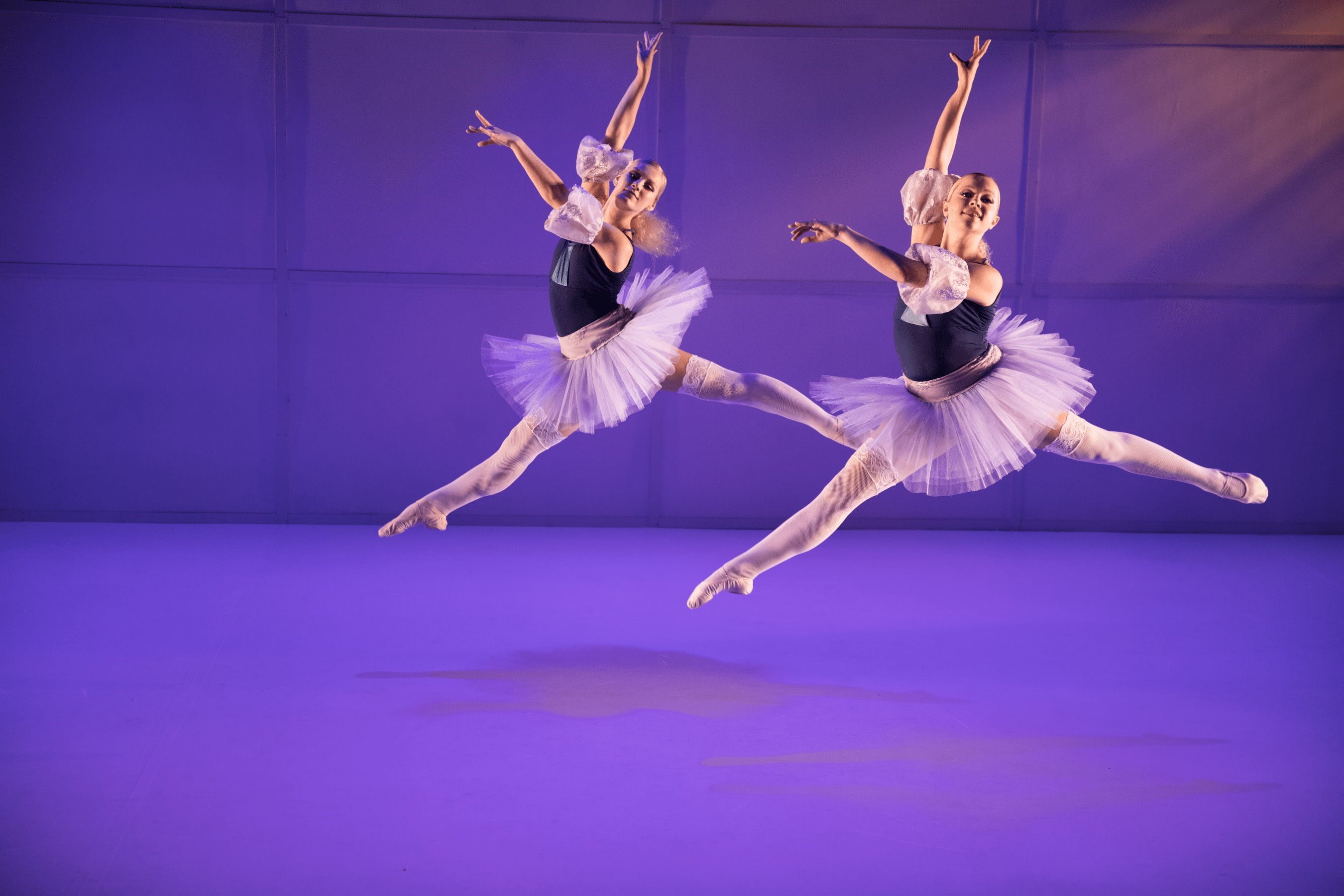 Two ballet dancers in matching attire synchronize a forward split leap
