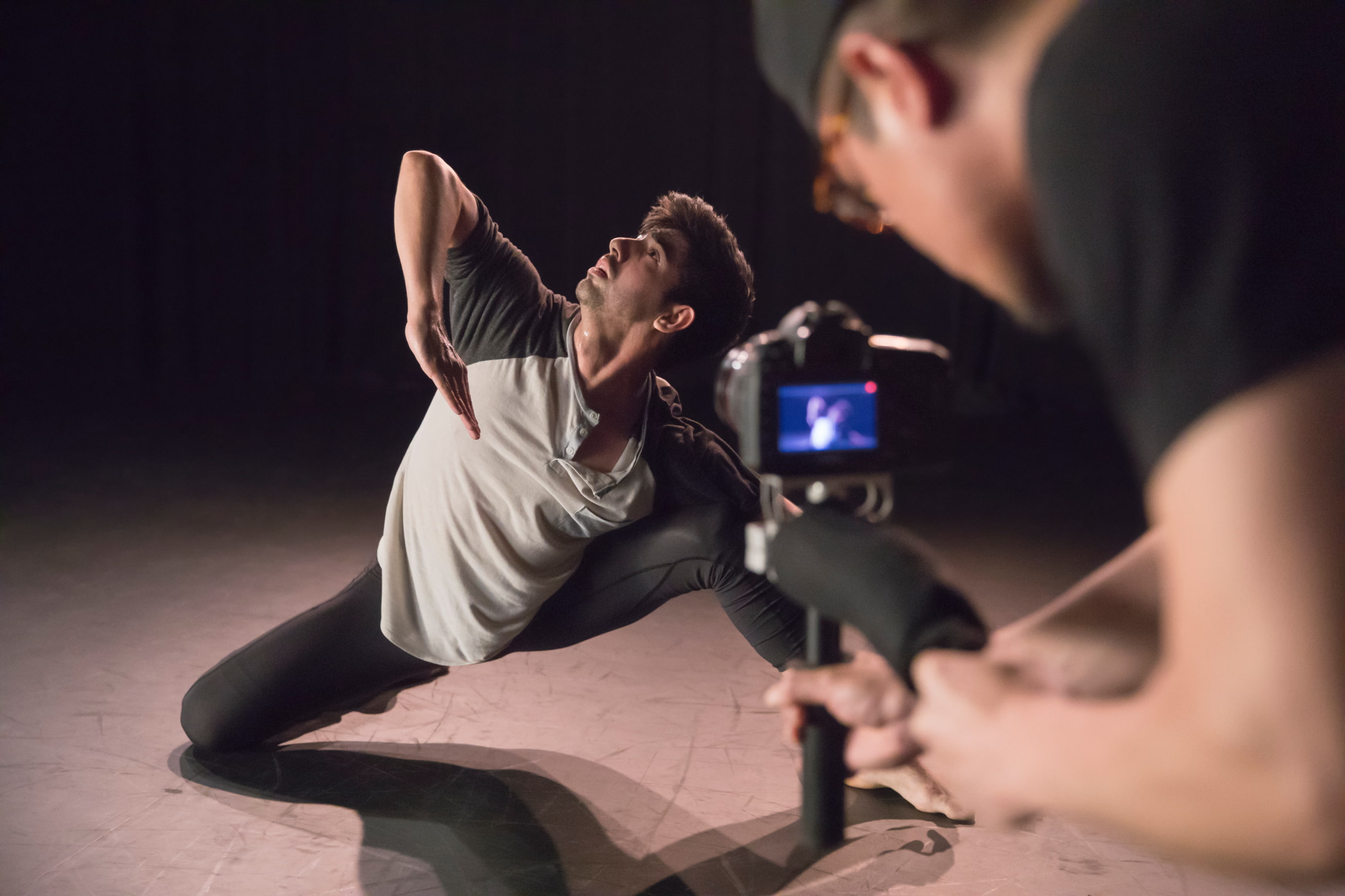 A dancer strikes a triangular pose with his elbow and gaze towards the sky as he is filmed