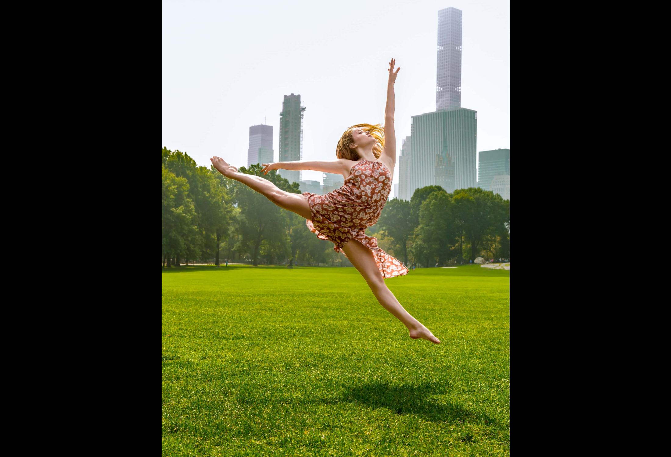 A dancer in a grassy field in central park does a split leap