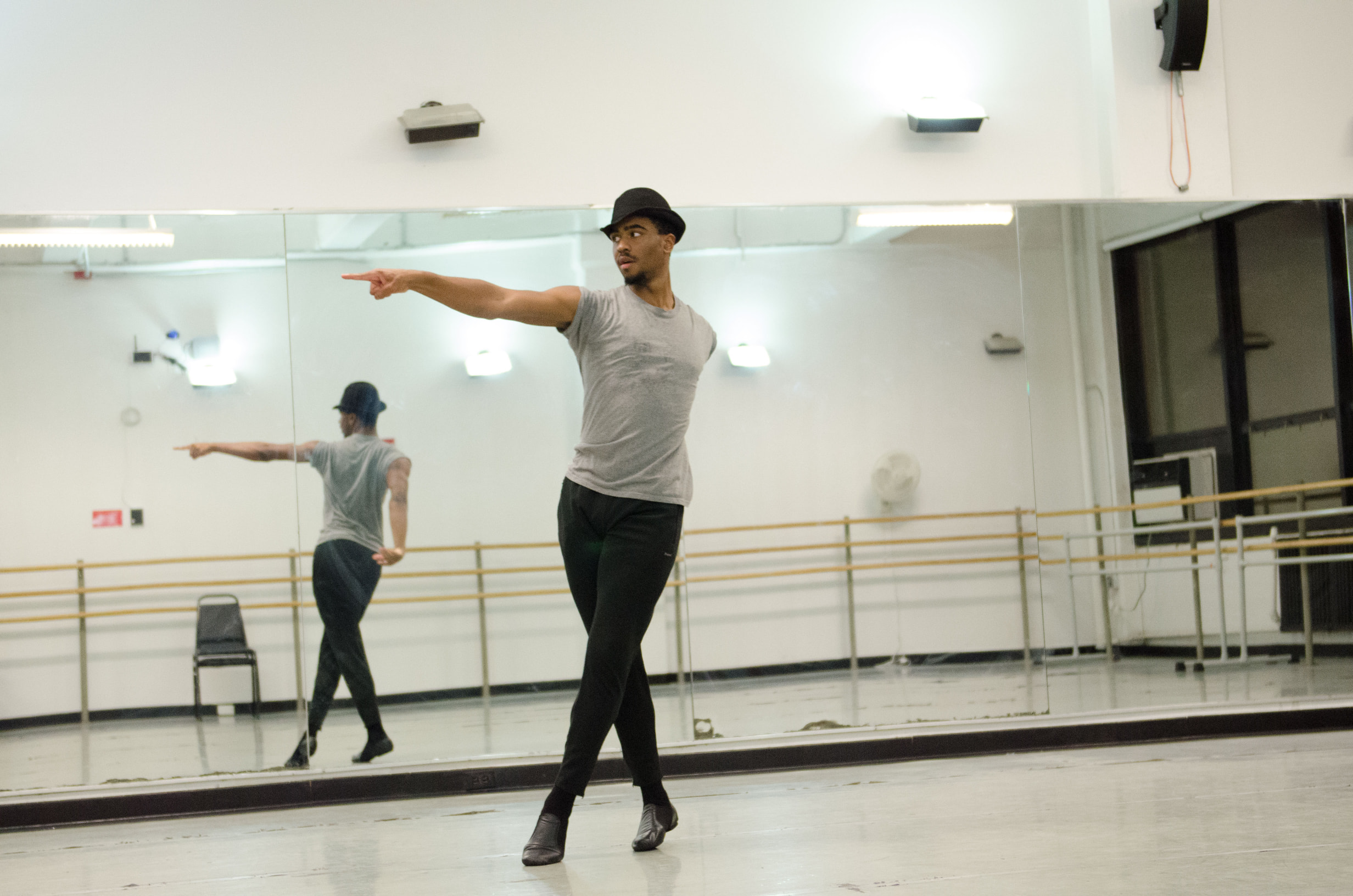 A solo dancer in a mirrored studio strikes a pointing pose