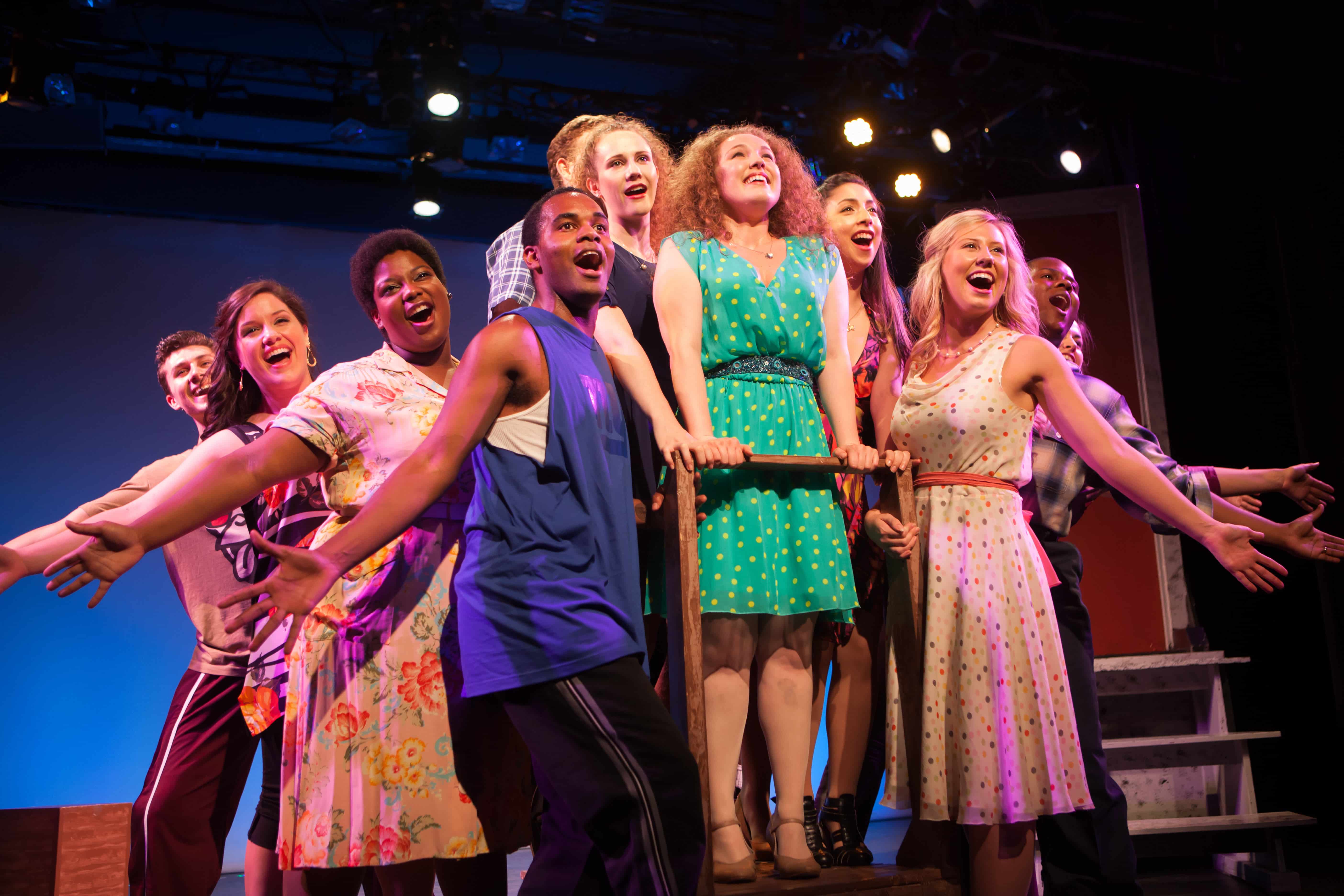 A beaming cast of performers gather and sing in unison