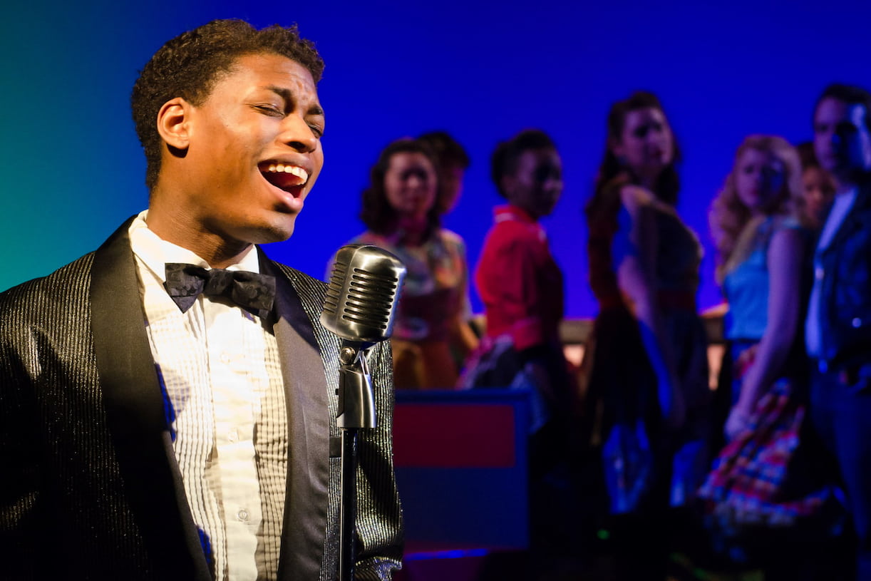 A singer in a tuxeduo sings with eyes closed into a condenser microphone