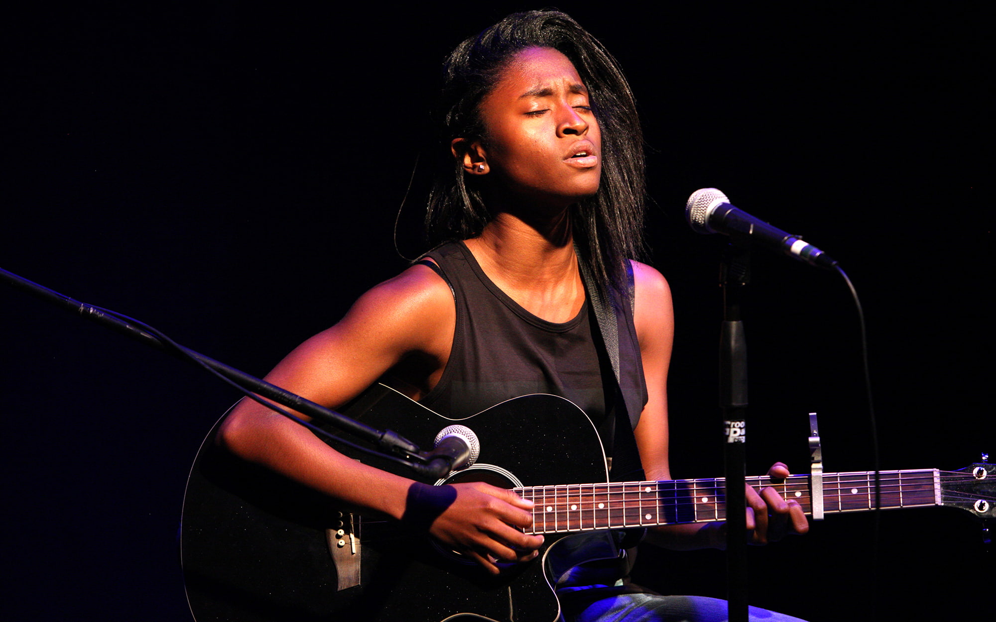 A person playing an acoustic guitar in front of a microphone.